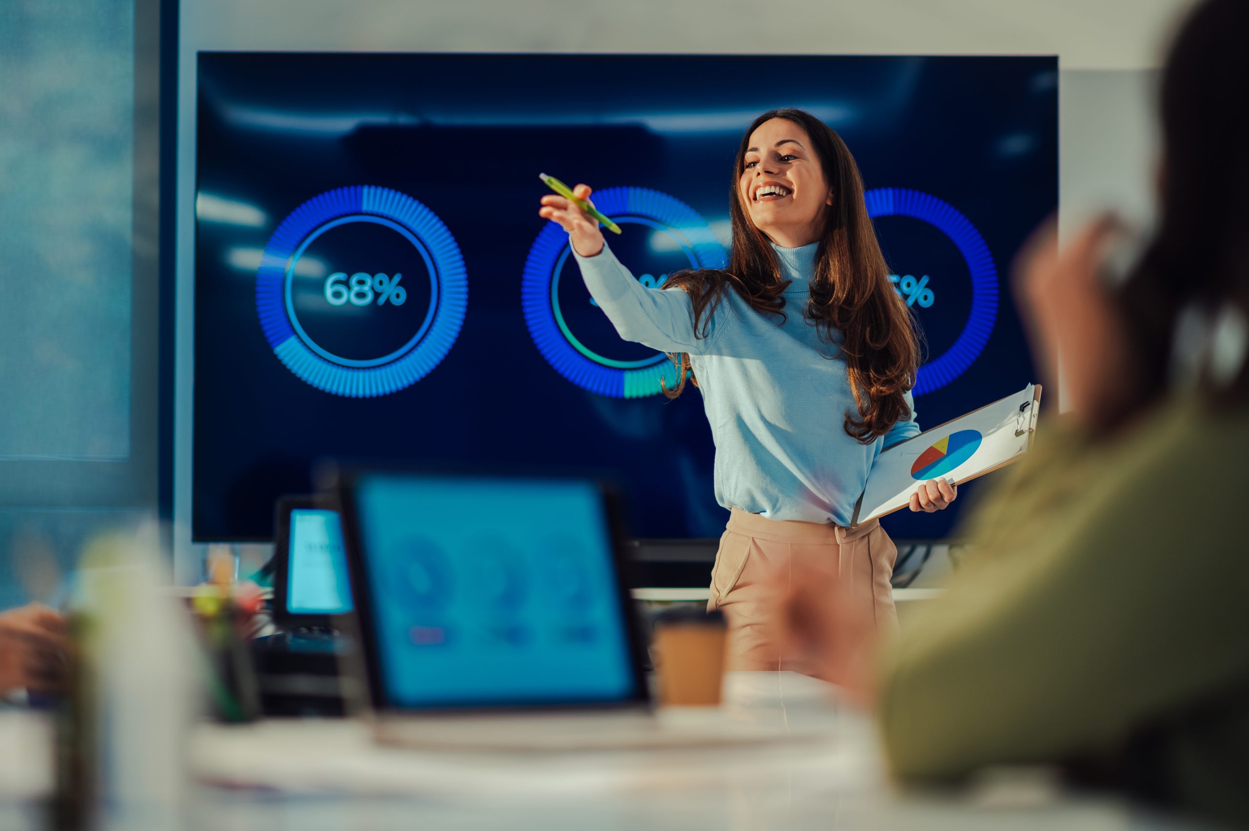 Muotokuva kaukasialaisesta naispuolisesta tiiminvetäjästä, joka esittelee projektin edistymistä kokouksessa ja osoittaa sormellaan toista kollegaa puhuessaan hänelle suoraan.